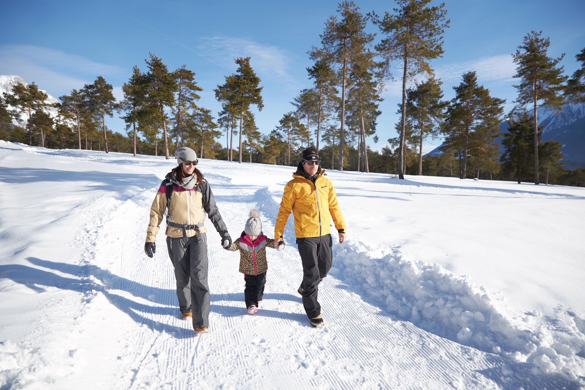 Parents and child stroll happily through a snowy winter landscape in the sunshine.